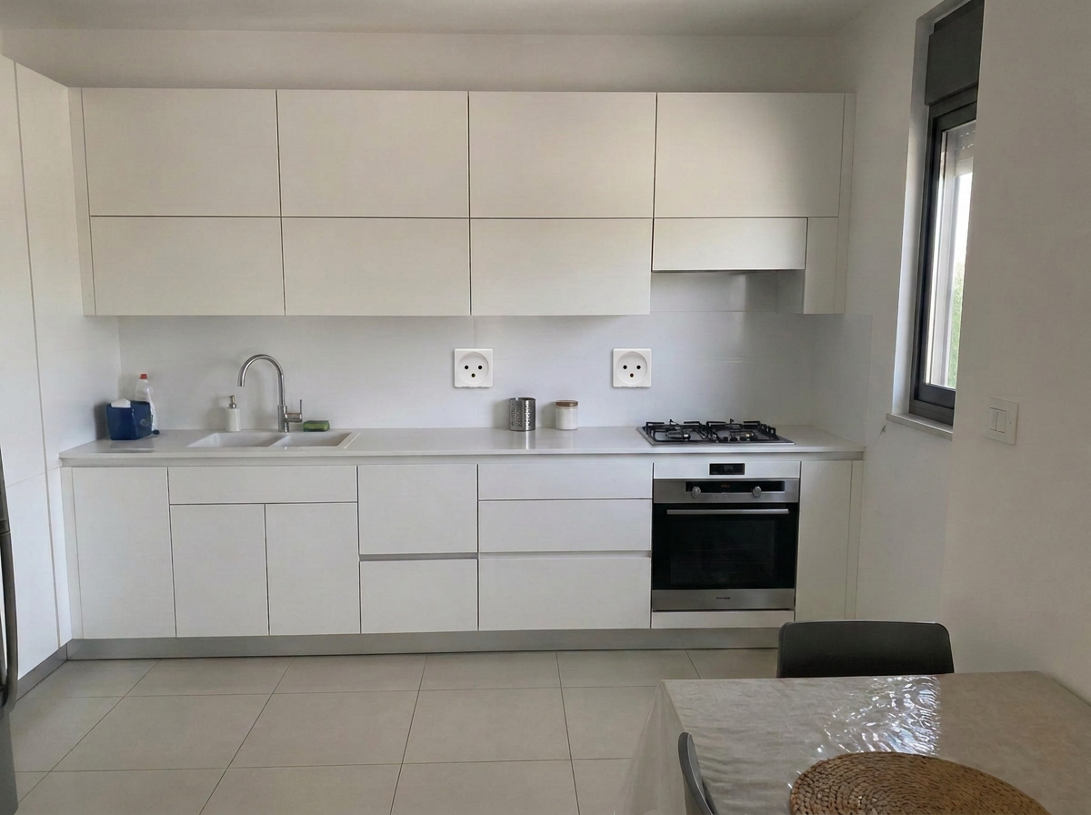 מטבח לבן ישר עם חזיתות חלקות ומשטח קוורץ לבן בדירה